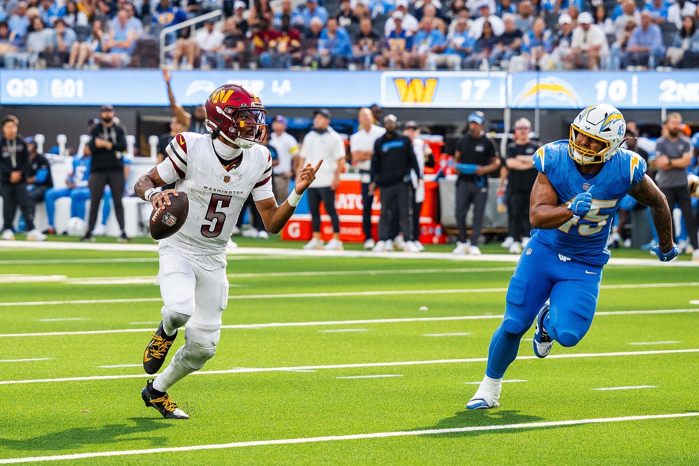 Jayden Daniels in a white Commanders No. 5 jersey scrambling with the ball as a Chargers defender chases