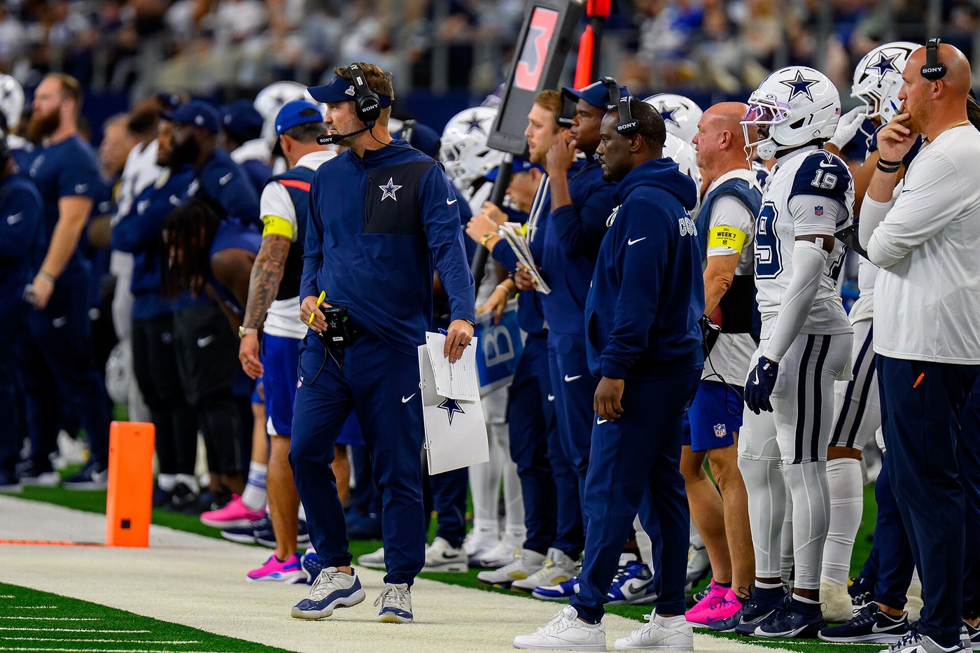 Brian Schottenheimer in a headset on the Cowboys sideline with players and staff