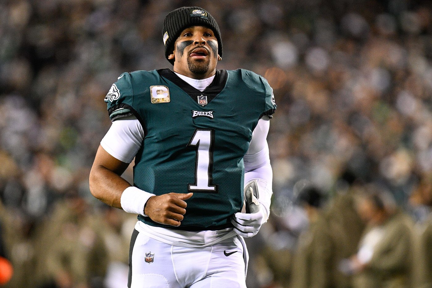 Jalen Hurts jogging on the field in a green Eagles No. 1 jersey and black beanie