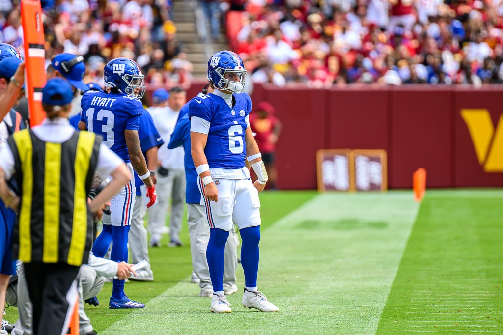 Jaxson Dart in a blue Giants No. 6 jersey on the sideline next to Jalin Hyatt